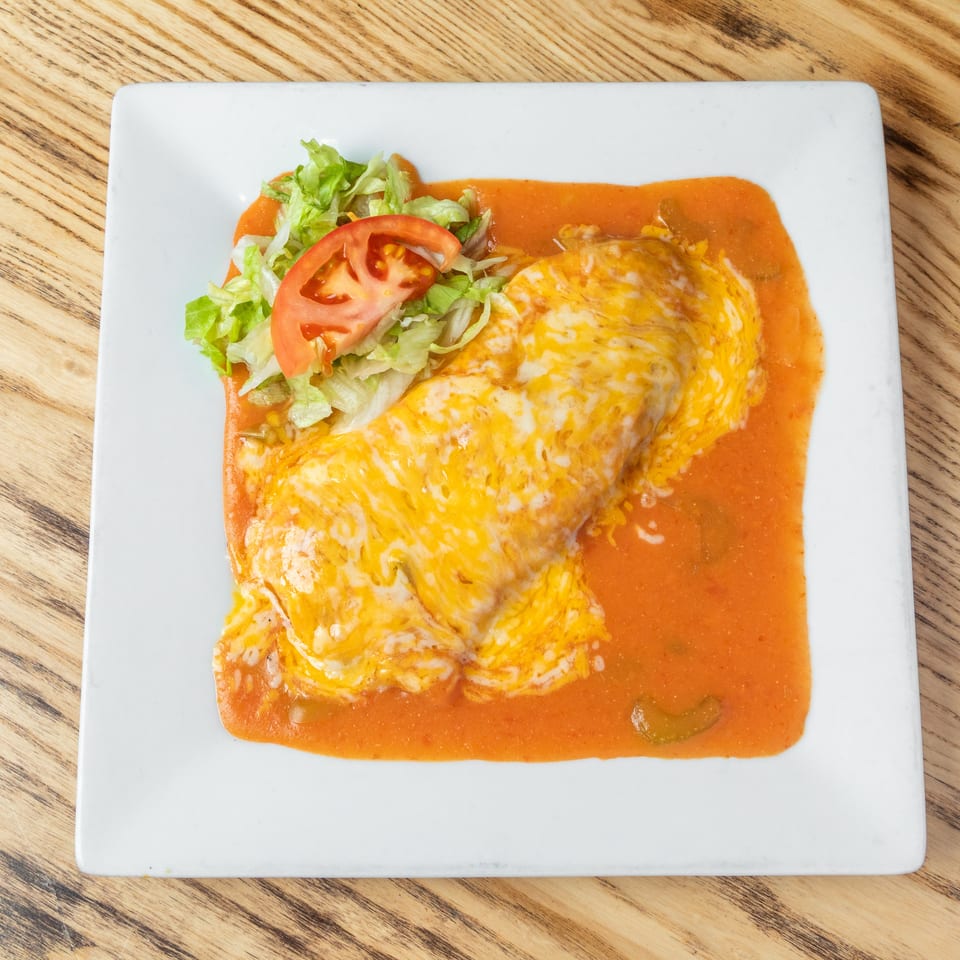 Cheese-covered enchiladas in red sauce served with shredded lettuce and sliced tomato on a white plate.