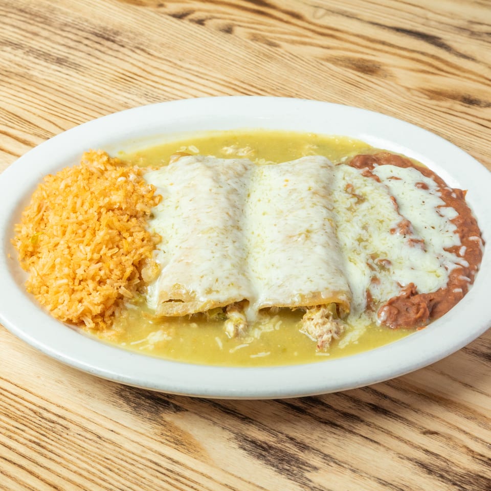 Cheese-covered enchiladas served with Mexican rice, refried beans, and green sauce on a white plate.