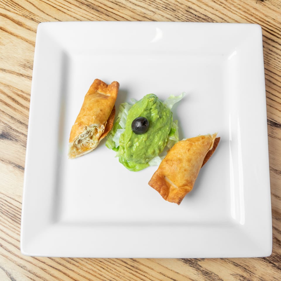 Two golden fried pastries served with lettuce, avocado, and a black olive on a white plate.