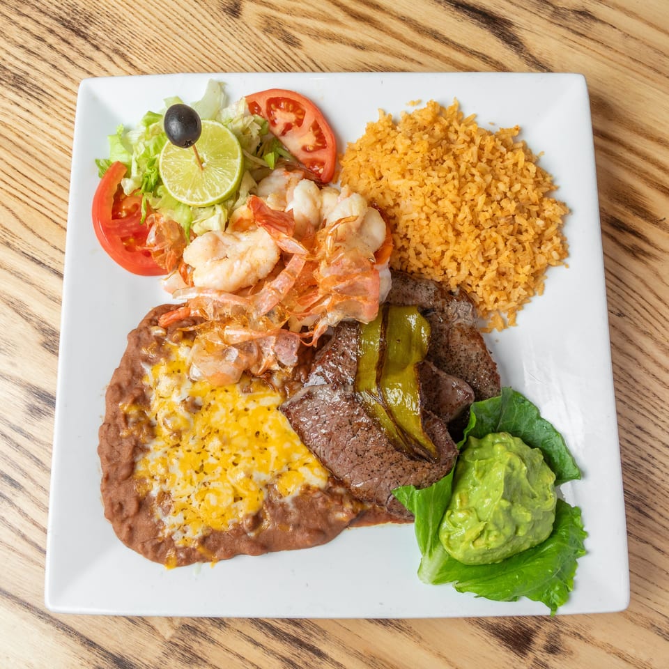 Mexican combo platter with grilled steak, shrimp, cheesy refried beans, Spanish rice, salad, guacamole, and vegetables.