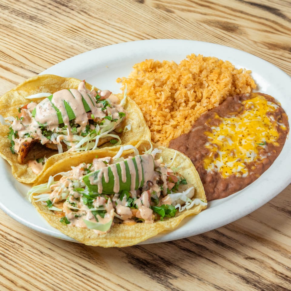 Mexican plate with two sauced tacos, Mexican rice, and cheese-topped refried beans on a white plate.