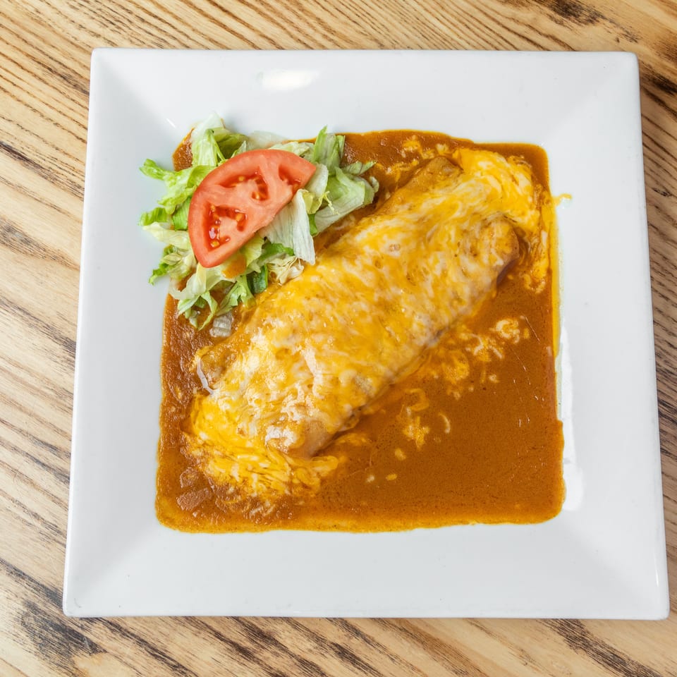 Cheese-covered enchilada smothered in red sauce, served with lettuce and sliced tomato on a white plate.