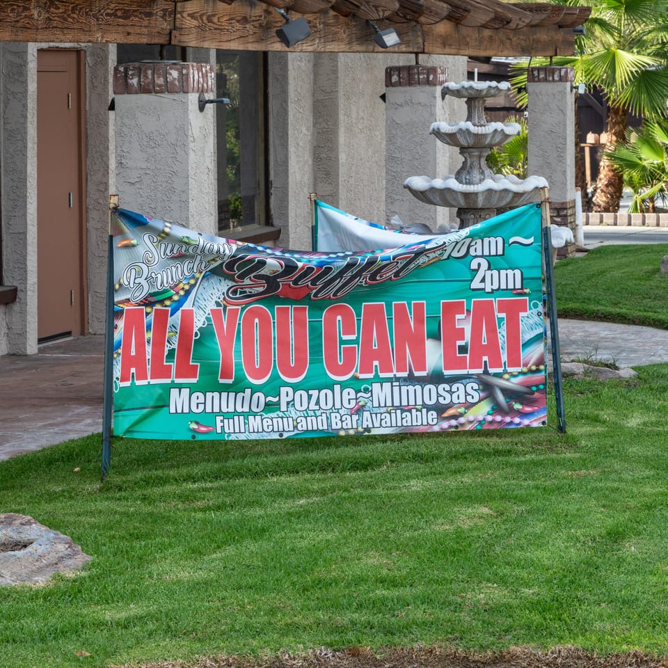 Restaurant entrance with a colorful Sunday brunch banner advertising all-you-can-eat menudo, pozole, mimosas, and a full menu and bar.