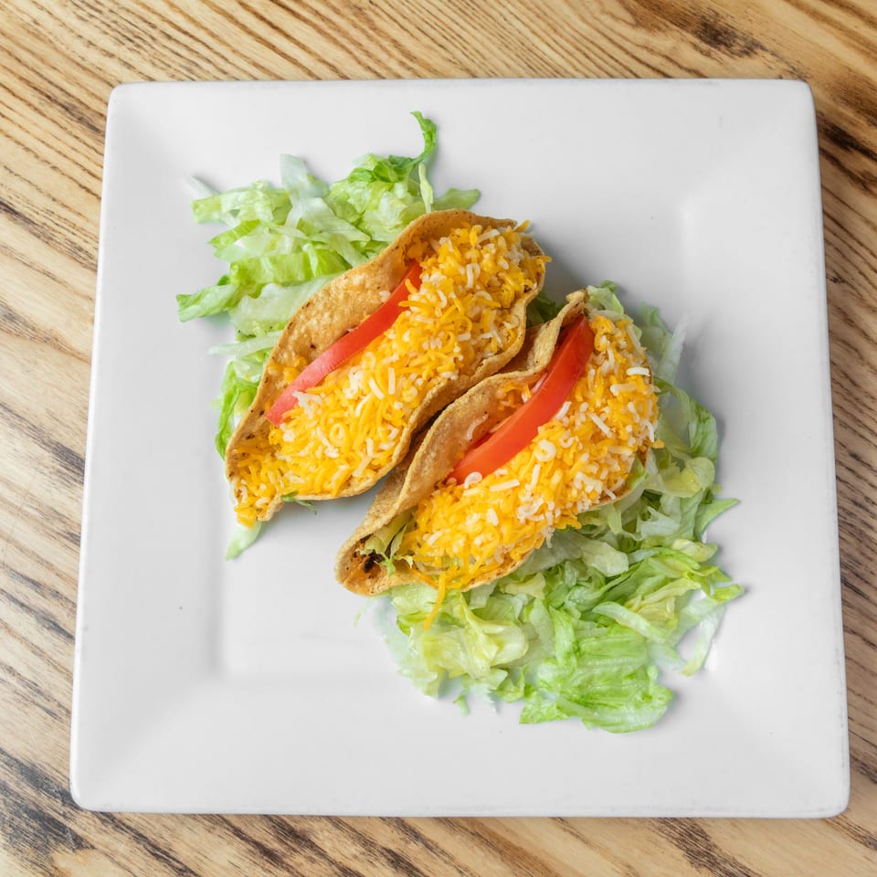 Three crispy tacos filled with rice, shredded cheese, and tomato slices, served over shredded lettuce on a white plate.