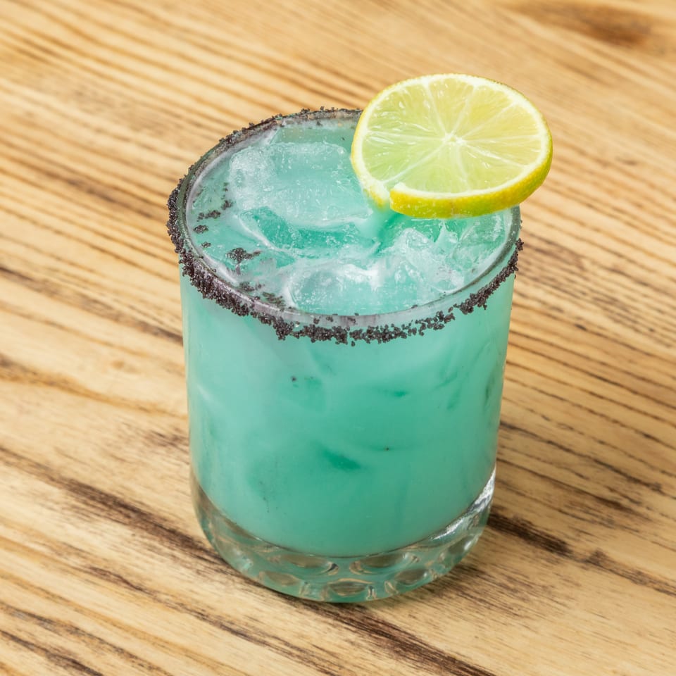 Blue frozen cocktail with a black-rimmed glass and lime slice on a wooden table.
