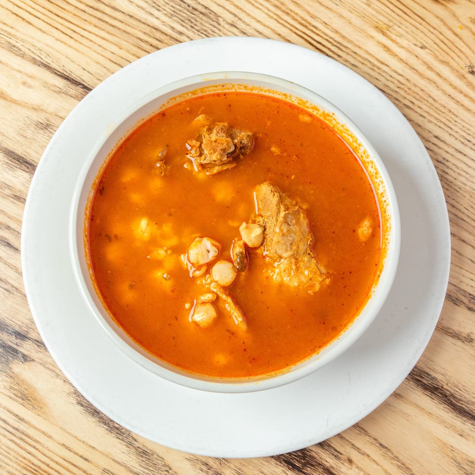Overhead view of a bowl of vibrant orange seafood soup with prawns and fish, served on a white plate atop a wooden table.