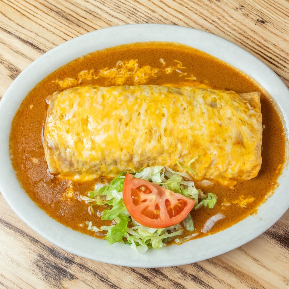 Cheese-covered burrito served in red chile sauce with shredded lettuce and tomato on a white plate.