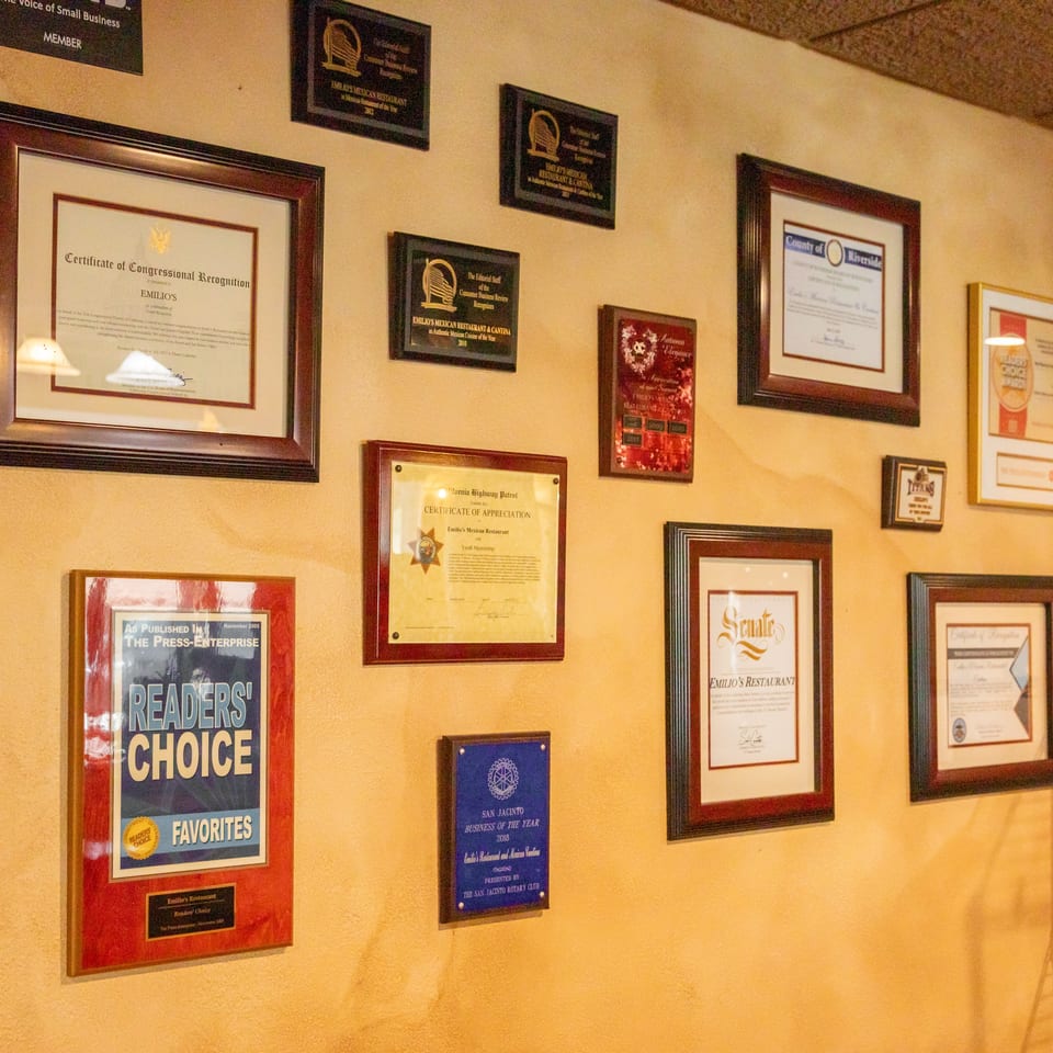 Restaurant wall displaying framed awards, certificates, plaques, and newspaper recognition for Emilio’s Mexican restaurant.