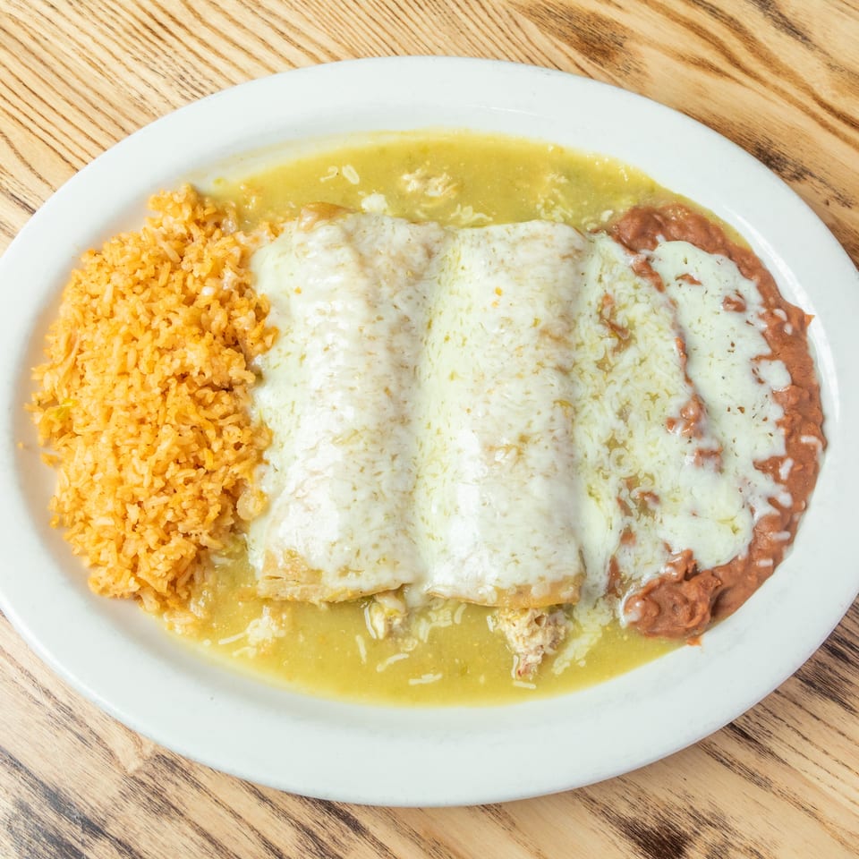 Cheese-covered enchiladas served with Mexican rice, refried beans, and green sauce on a white plate.
